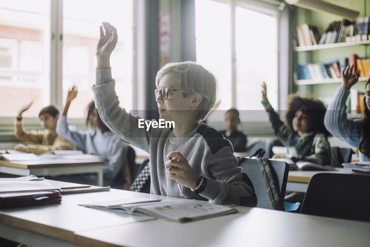 Boy with hand raised attending lecture in classroom