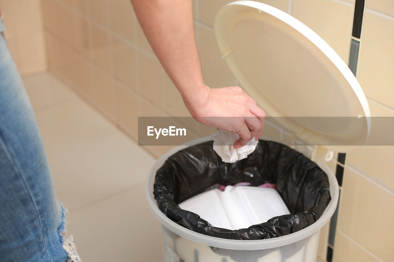 Midsection of woman putting garbage in bin at home