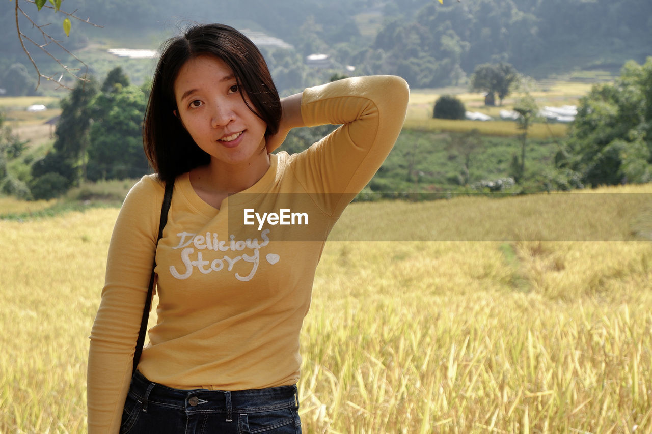 PORTRAIT OF SMILING YOUNG WOMAN STANDING ON LAND