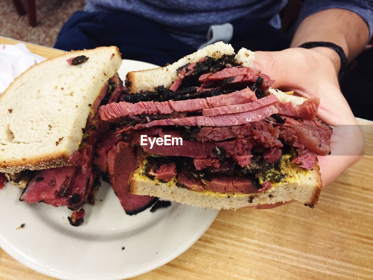 Cropped image of hand holding pastrami sandwich over table