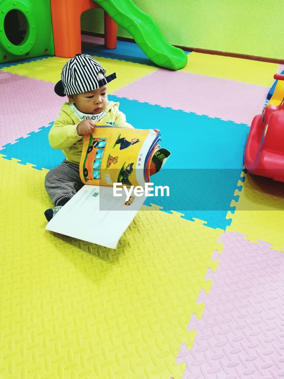 HIGH ANGLE VIEW OF BOY SITTING ON MULTI COLORED BOOK