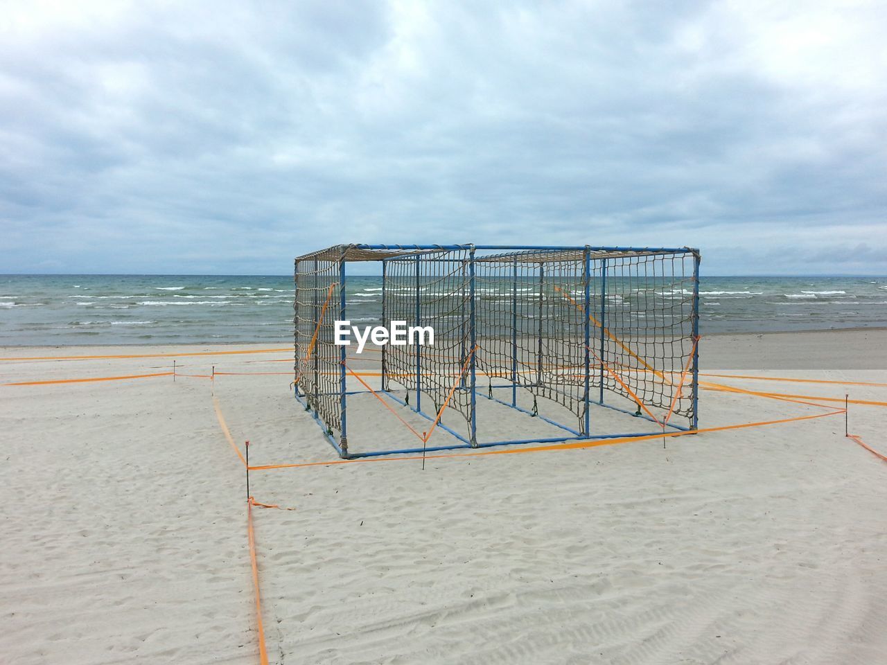 Cage at beach against cloudy sky