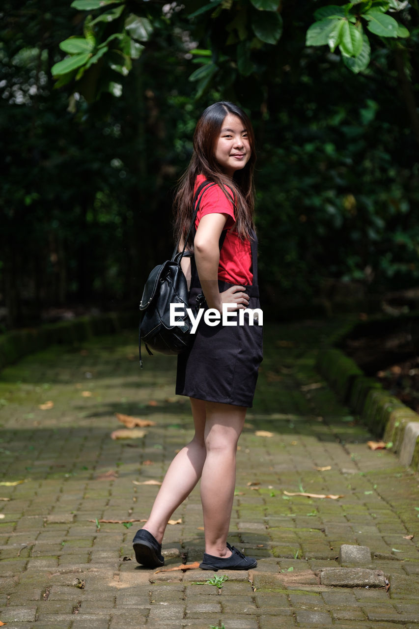 Full length of smiling young woman standing on footpath at park