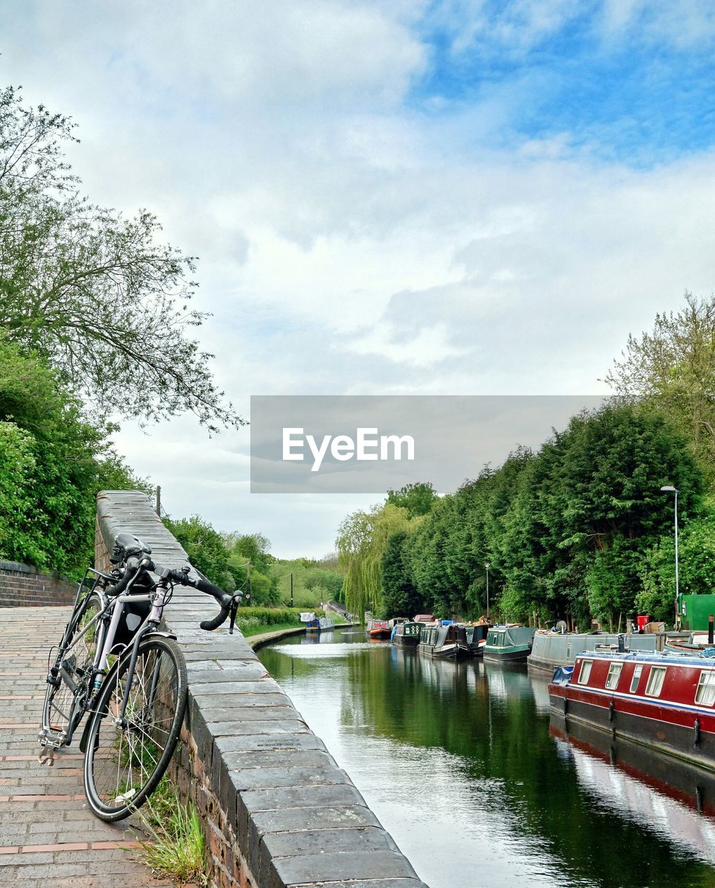 Bicycle parked by canal against cloudy sky