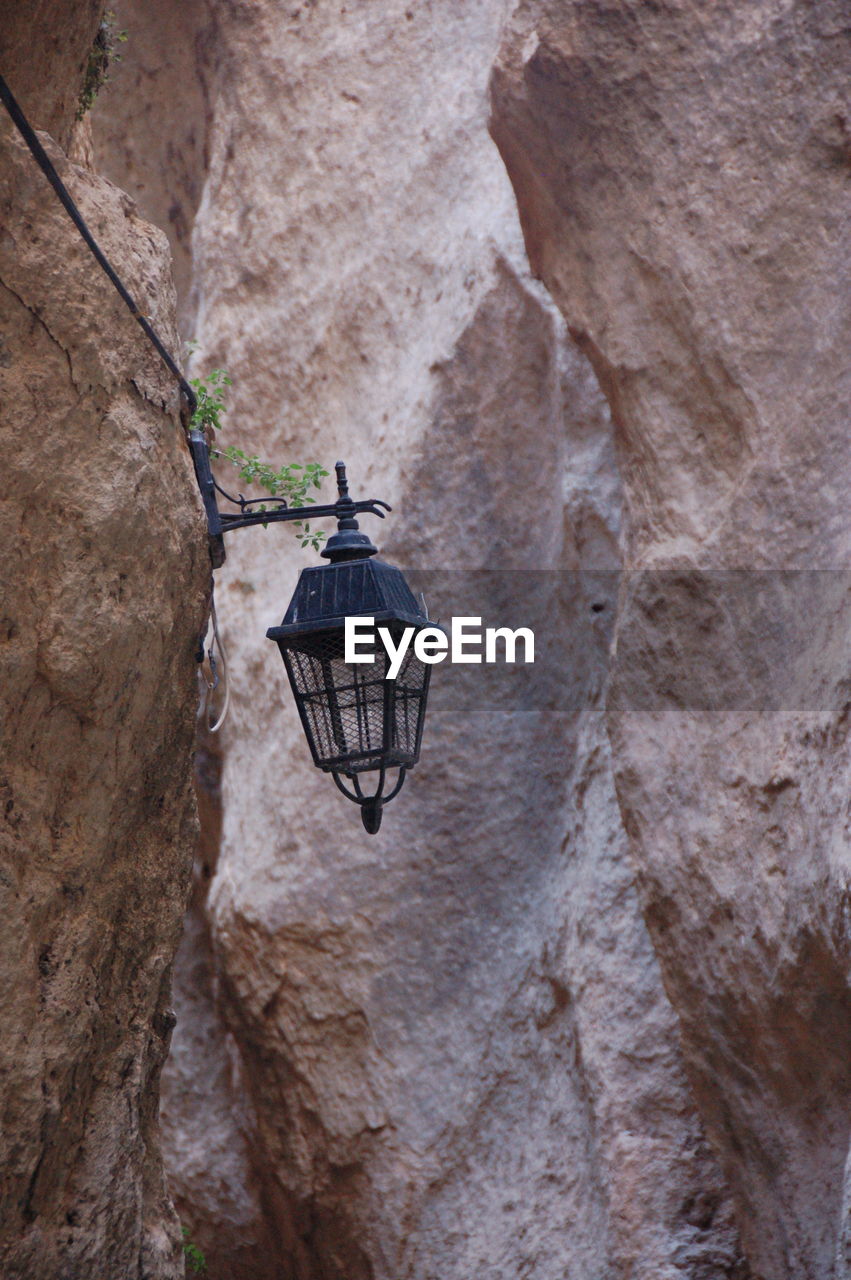 LOW ANGLE VIEW OF ELECTRIC LAMP HANGING ON ROCK AGAINST MOUNTAINS