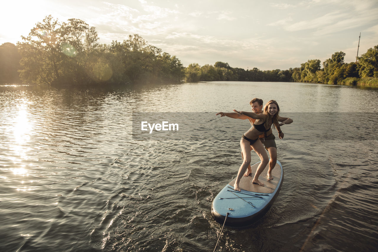 Young couple enjoying summer at the lake, standing on a paddleboard