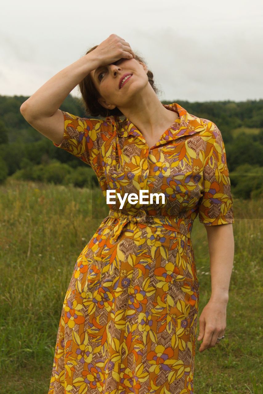 Woman with hand in hair standing on land against sky