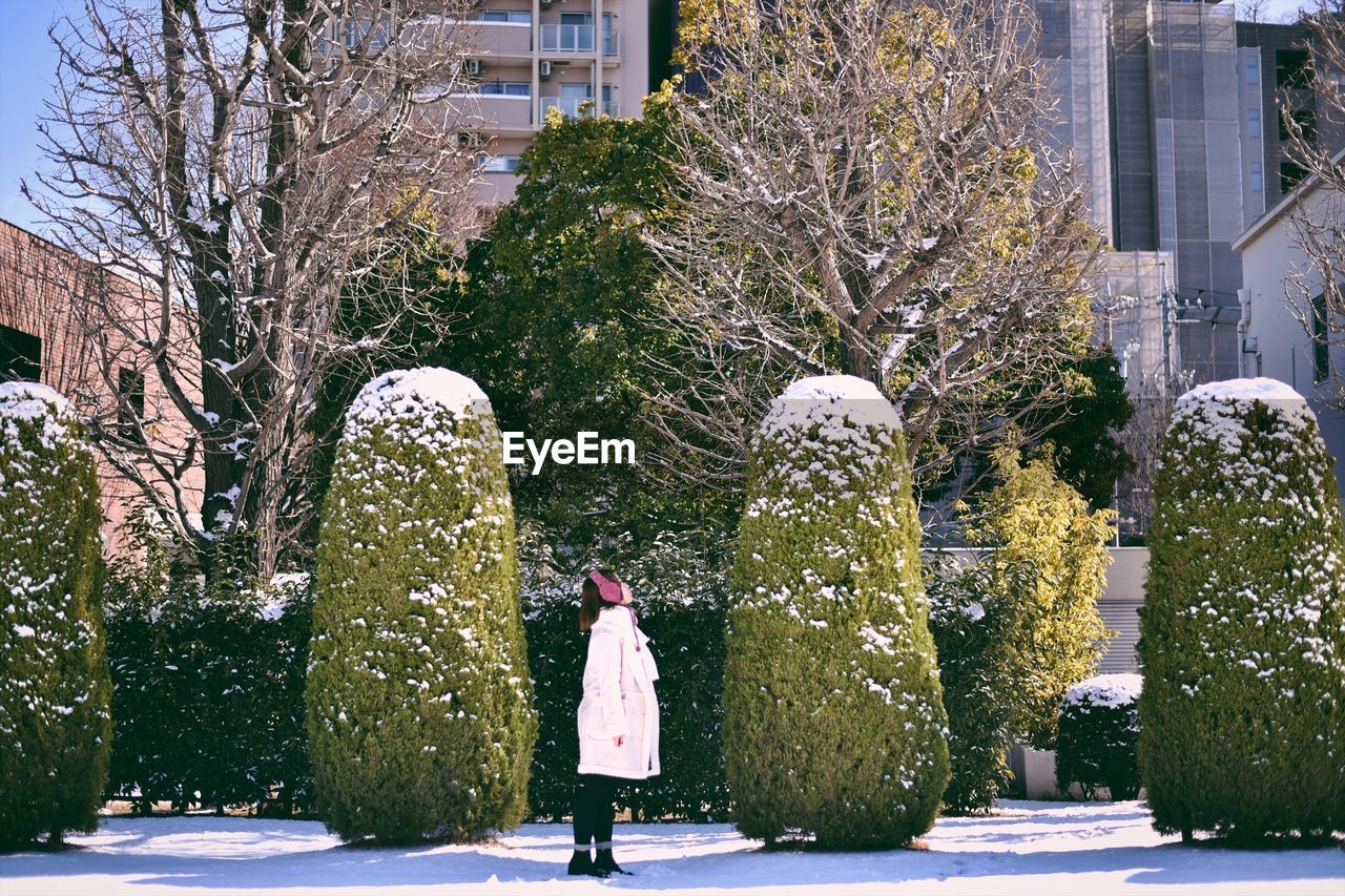 Side view of woman standing by snow covered tree