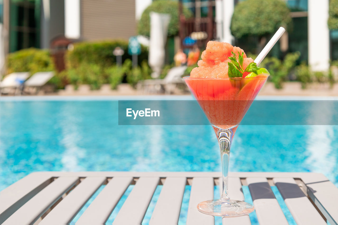 Fresh red cocktail with ice in glass on swimming pool. tropical juice on luxury 