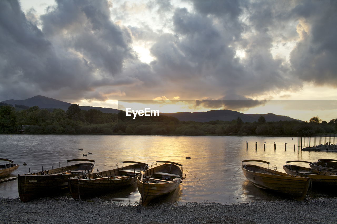 Boats moored at beach against cloudy sky during sunset