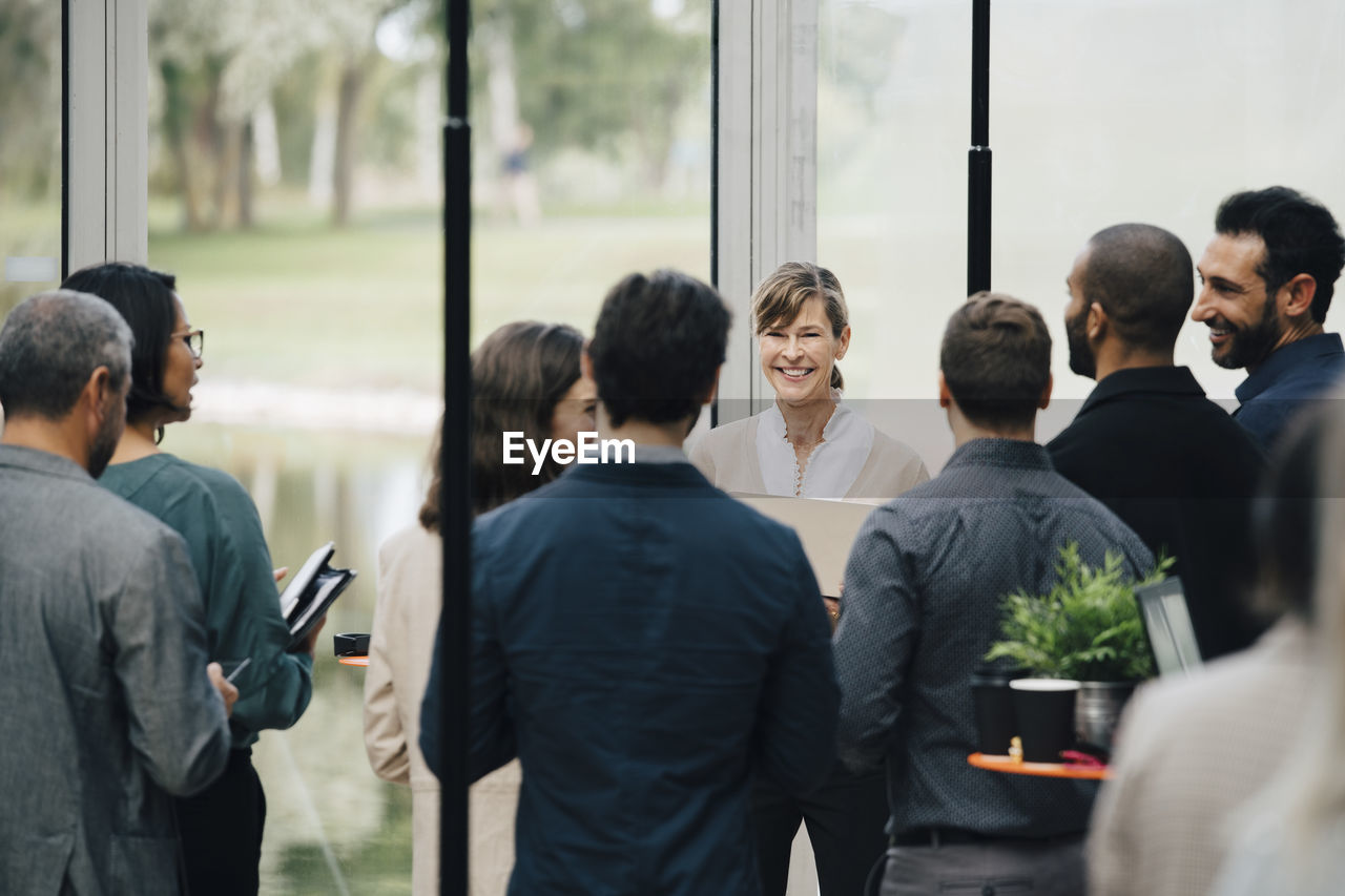 Smiling mature female entrepreneur talking to coworkers in office workshop