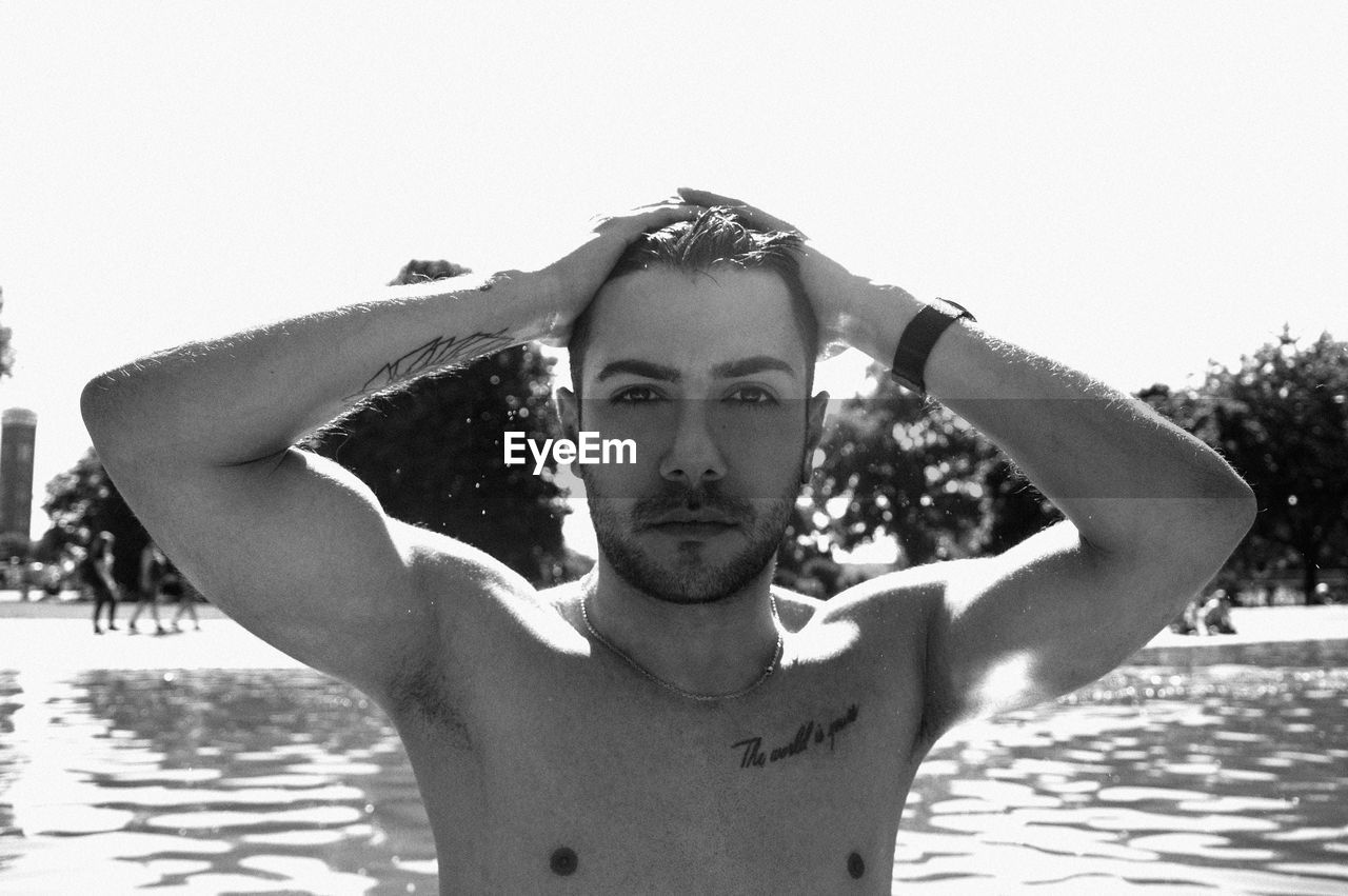 Portrait of shirtless man with hand in hair at beach