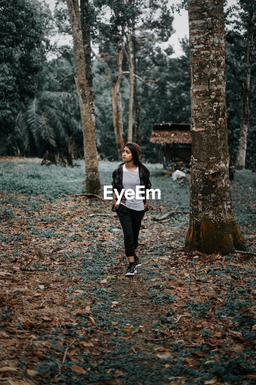 Full length of woman standing by tree trunk in forest