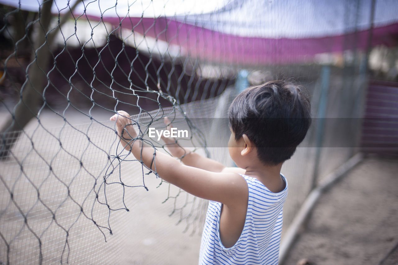 Boy standing by chainlink fence