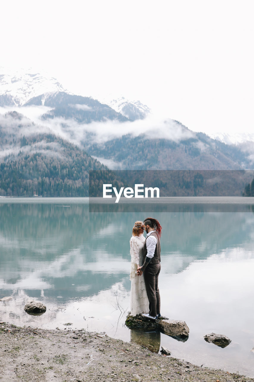 A loving married couple the bride and groom in suits celebrate wedding near the mountains and water