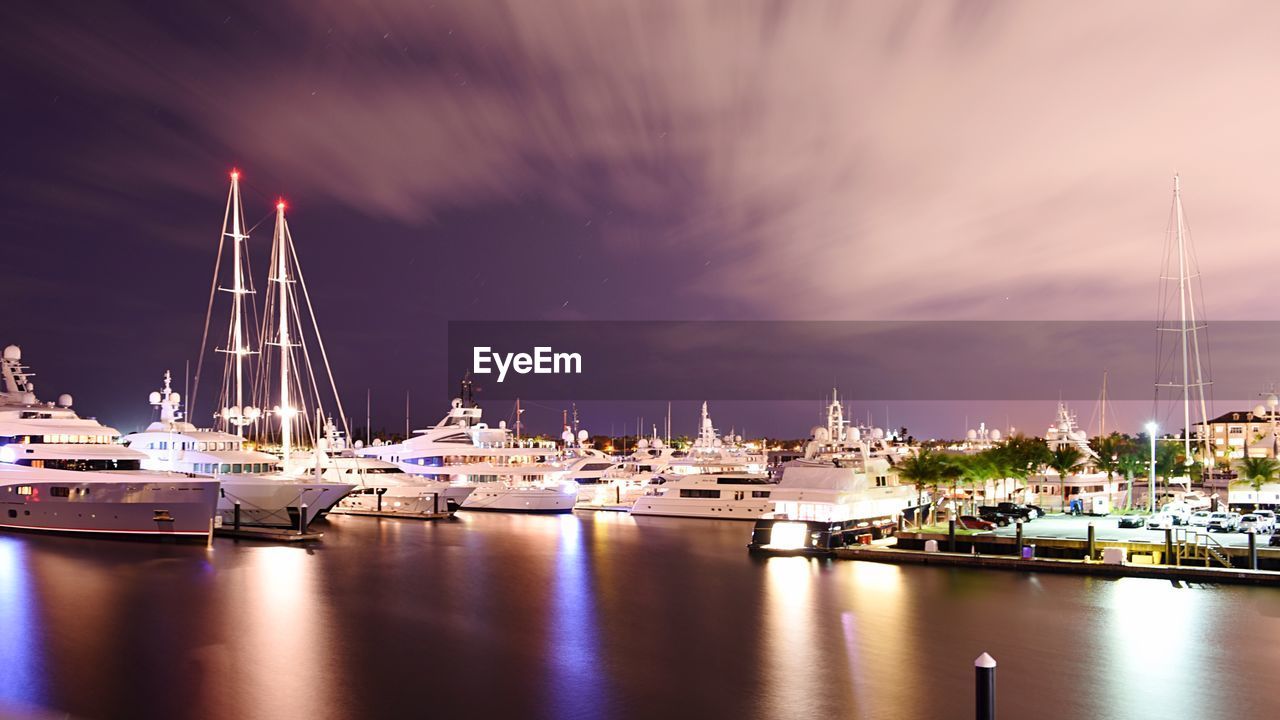 Boats moored at illuminated harbor against sky during dusk