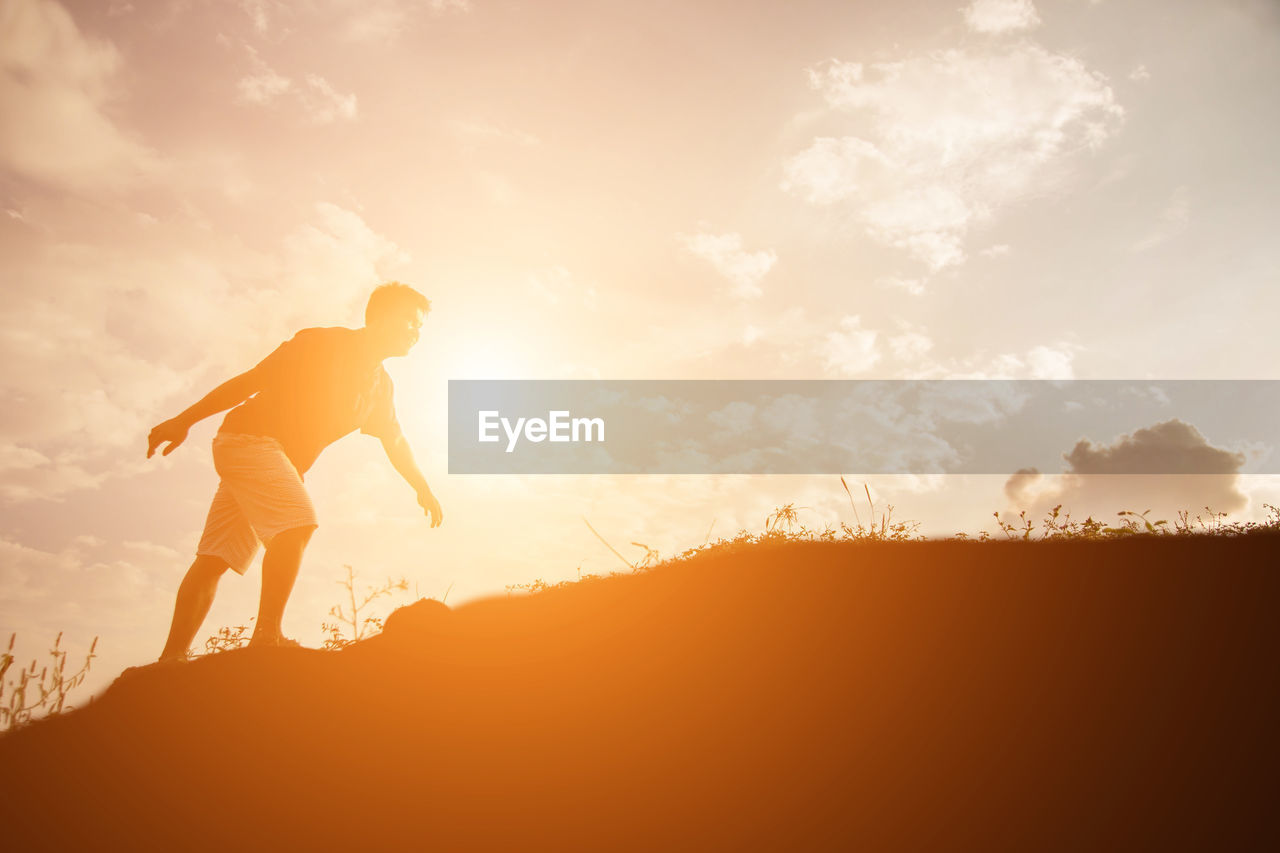 SILHOUETTE MAN STANDING AGAINST ORANGE SKY