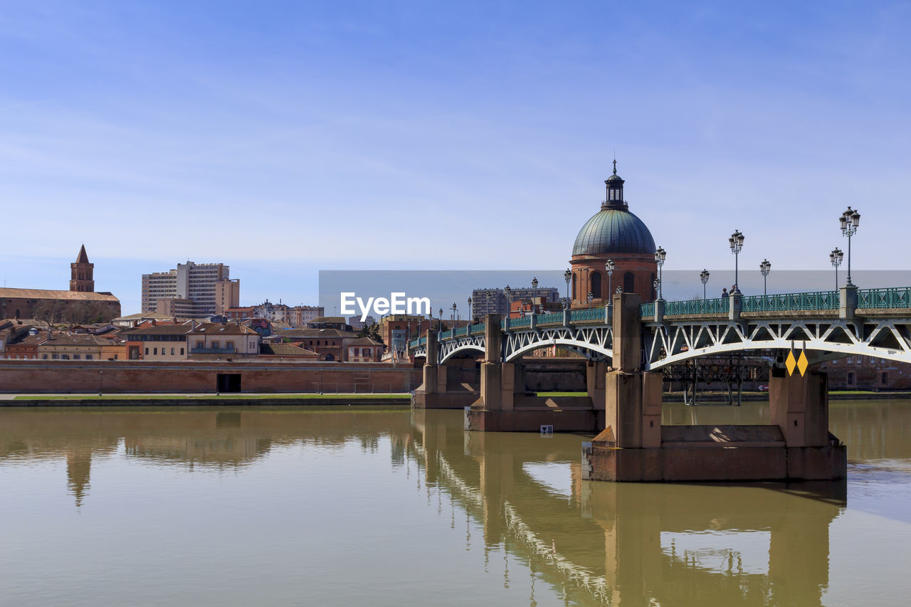Bridge over river by buildings against sky in city