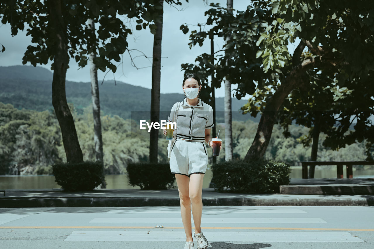 Confident young women hand holding ice beverage walking crossing street