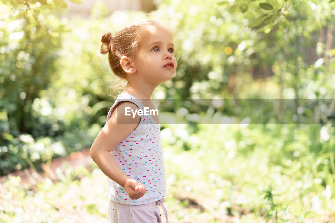 Girl looking away while standing against plants