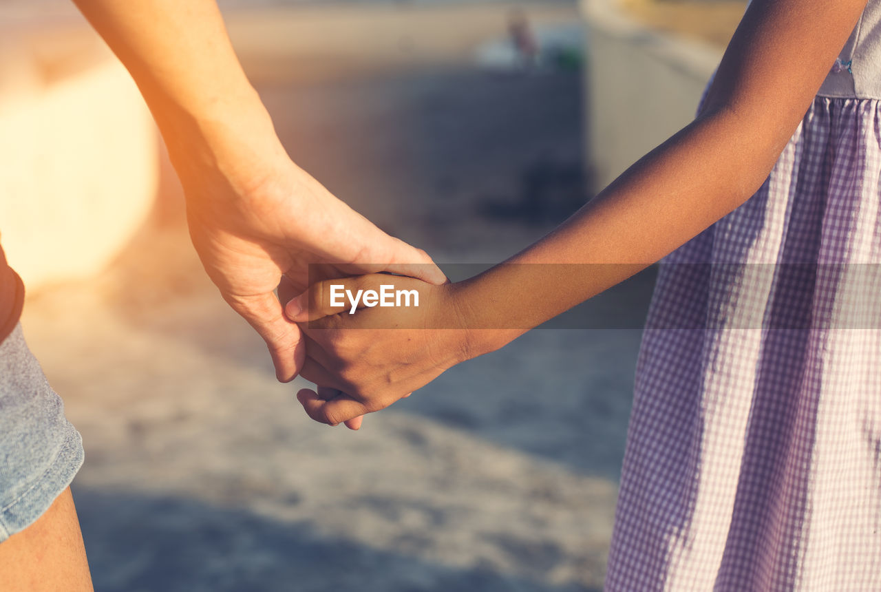 Midsection of mother and daughter with holding hands standing outdoors