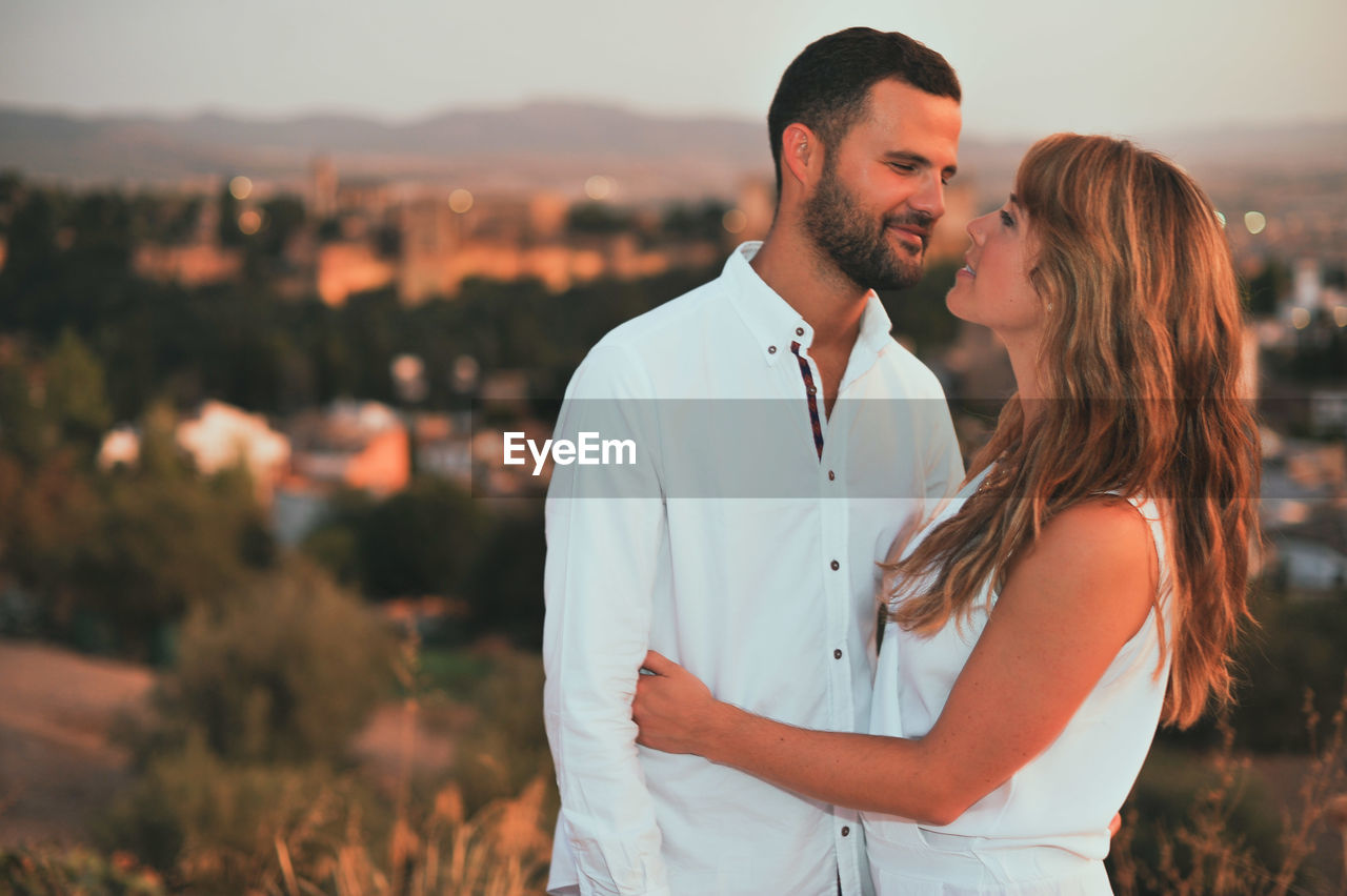 Smiling couple standing against cityscape during sunset