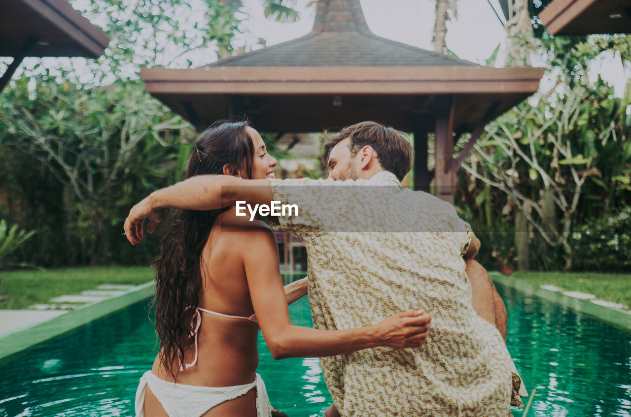 COUPLE KISSING IN SWIMMING POOL AGAINST TREES