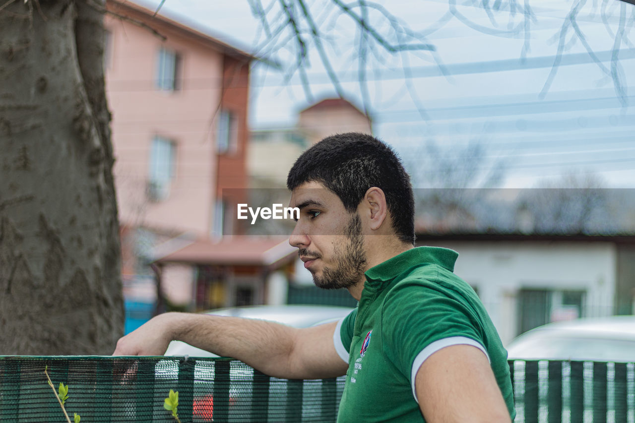 PORTRAIT OF YOUNG MAN LOOKING AWAY WHILE STANDING OUTDOORS