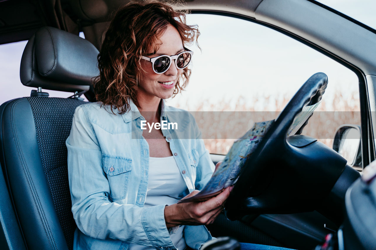 Smiling woman wearing sunglasses reading map in car
