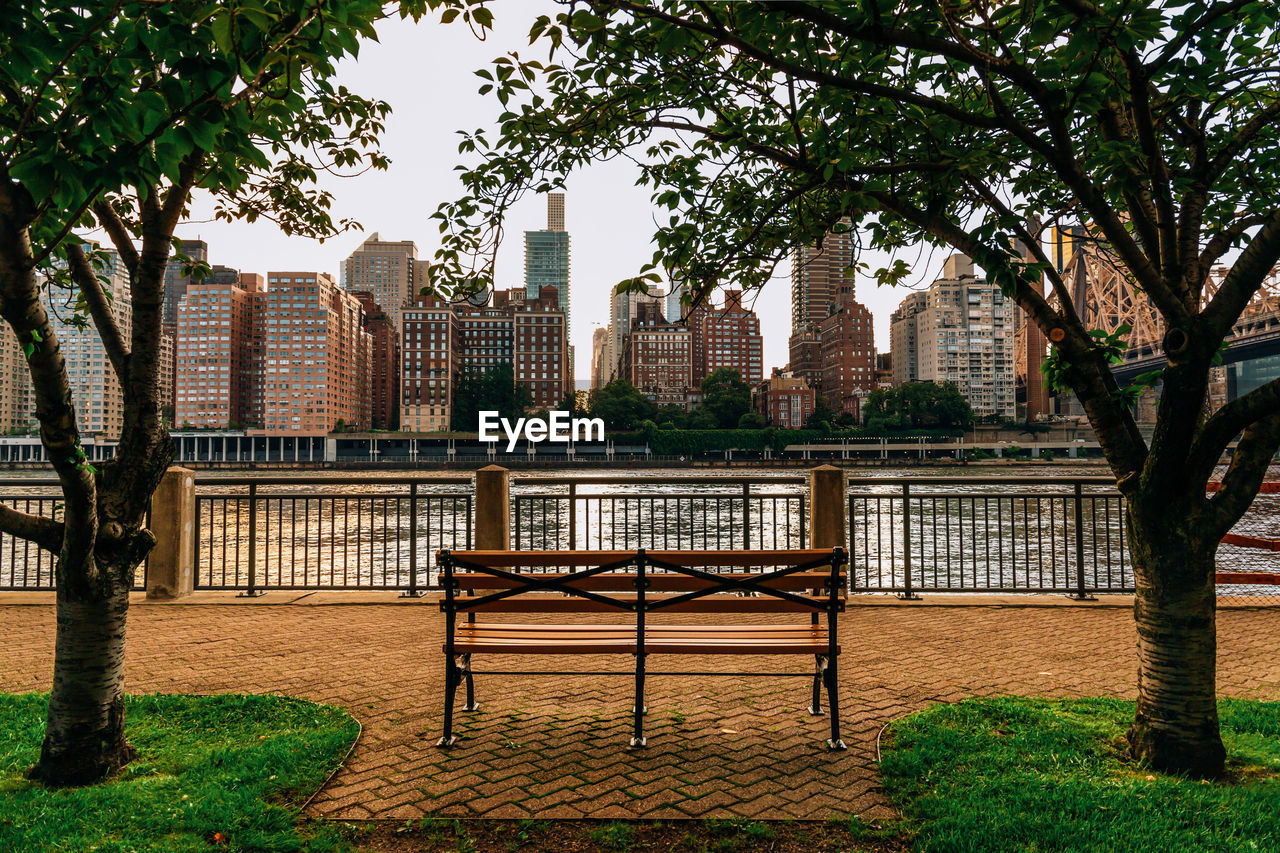 PARK BENCH BY BUILDINGS AGAINST SKY