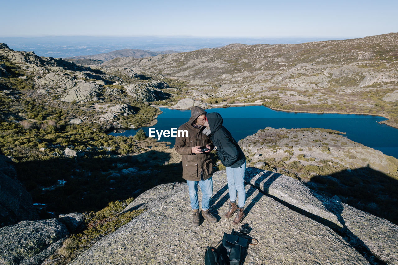 Couple kissing while standing on mountain against clear sky