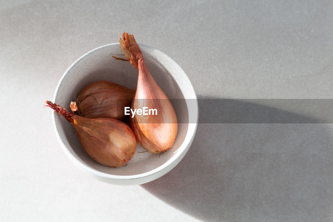 Raw dry shallots in lightly speckled white bowl on ceramic background