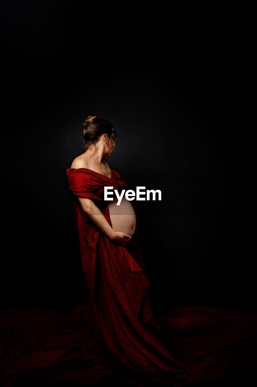 Portrait of young pregnant woman standing against black background