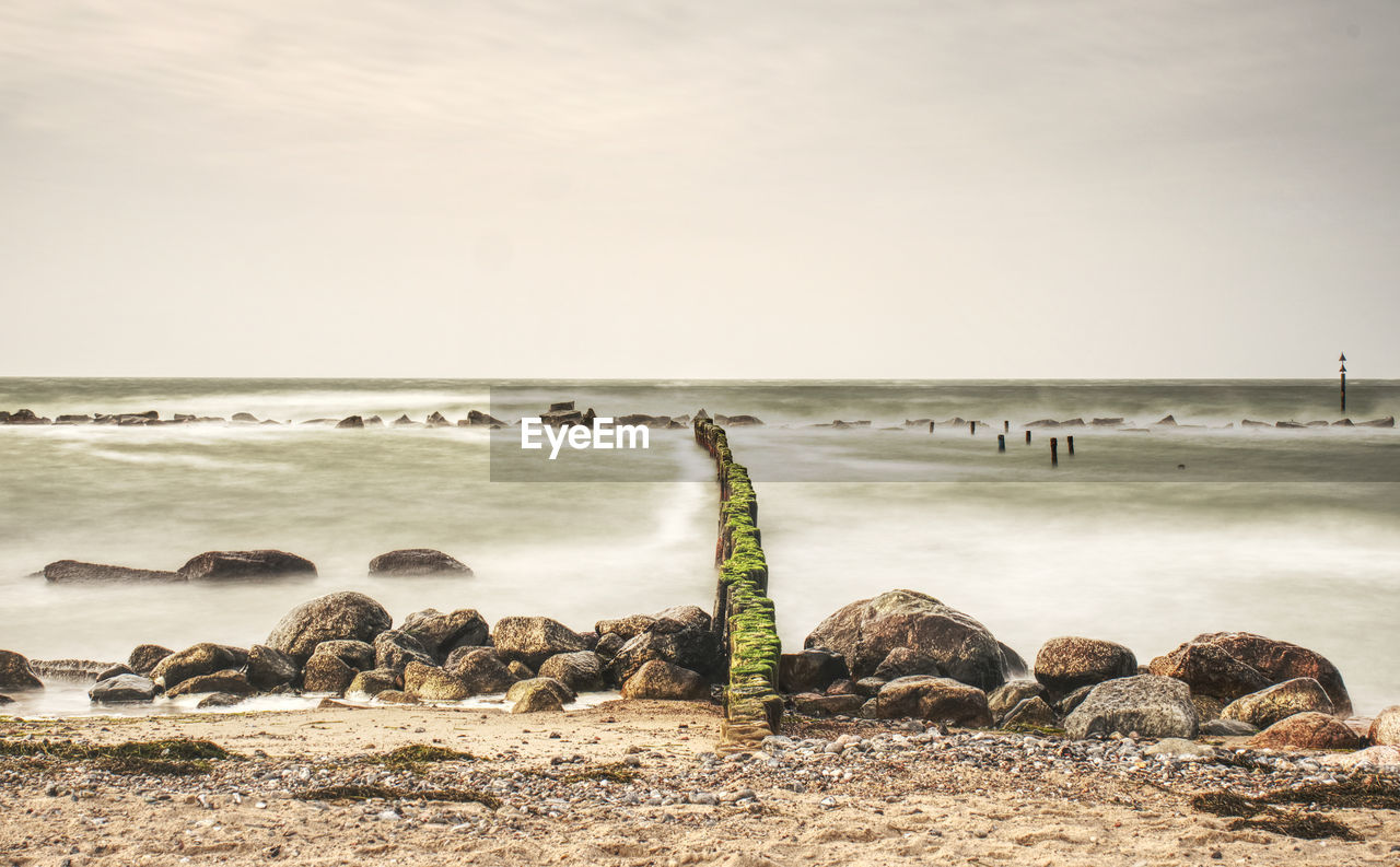 Seascape with breakwaters at sunset with foamy waves on beach and heavy cloud cover