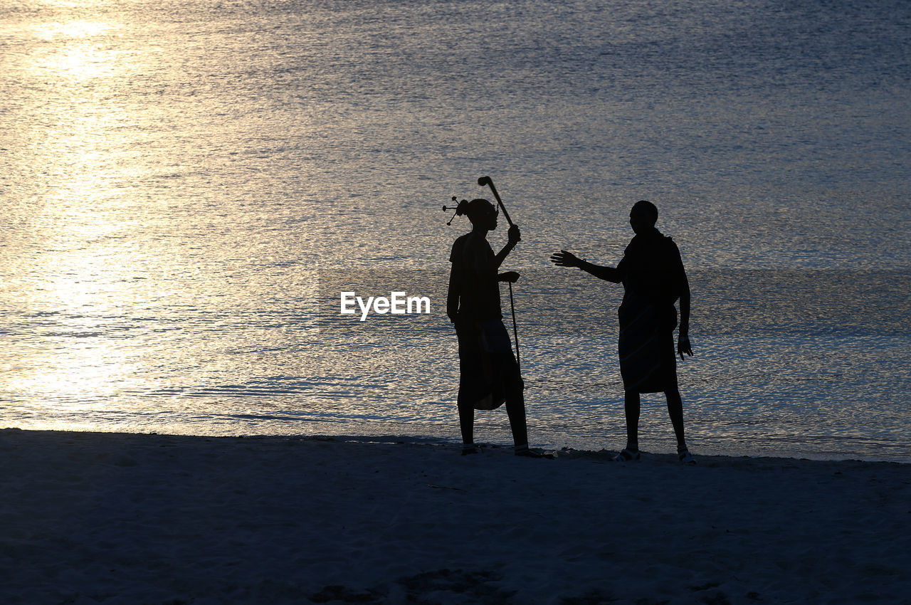 Silhouette men standing on shore at beach during sunset