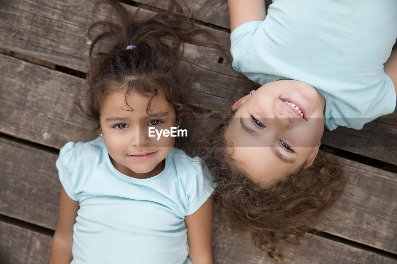 High angle portrait of cute sisters lying on deck