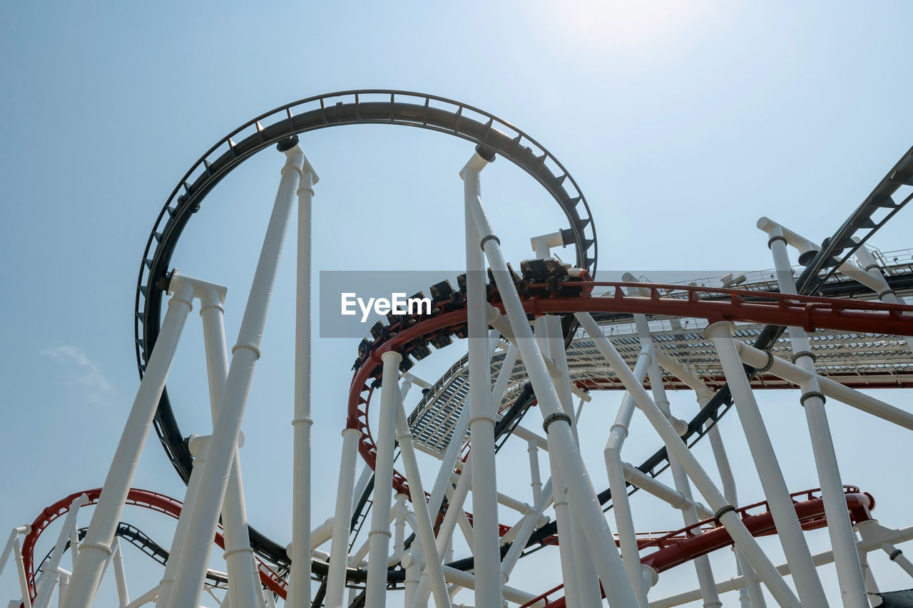 People on roller coaster in amusement park against blue sky and sun