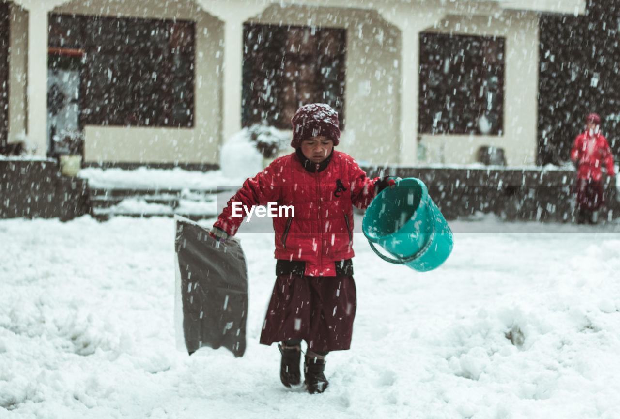 Boy wearing jacket holding bucket while walking in snow