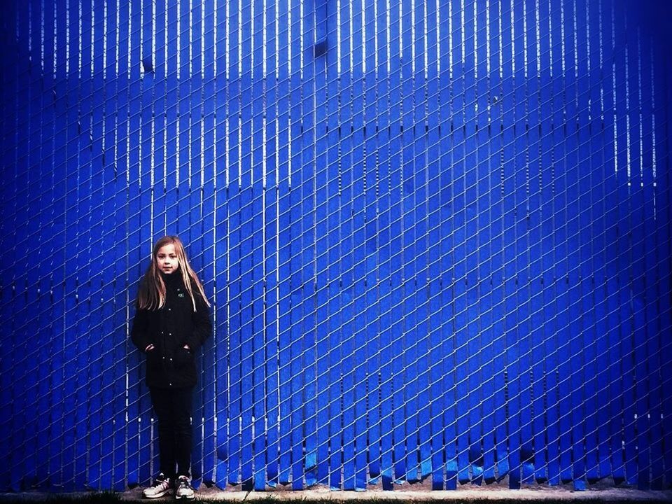 Full length of a girl standing against blue wall