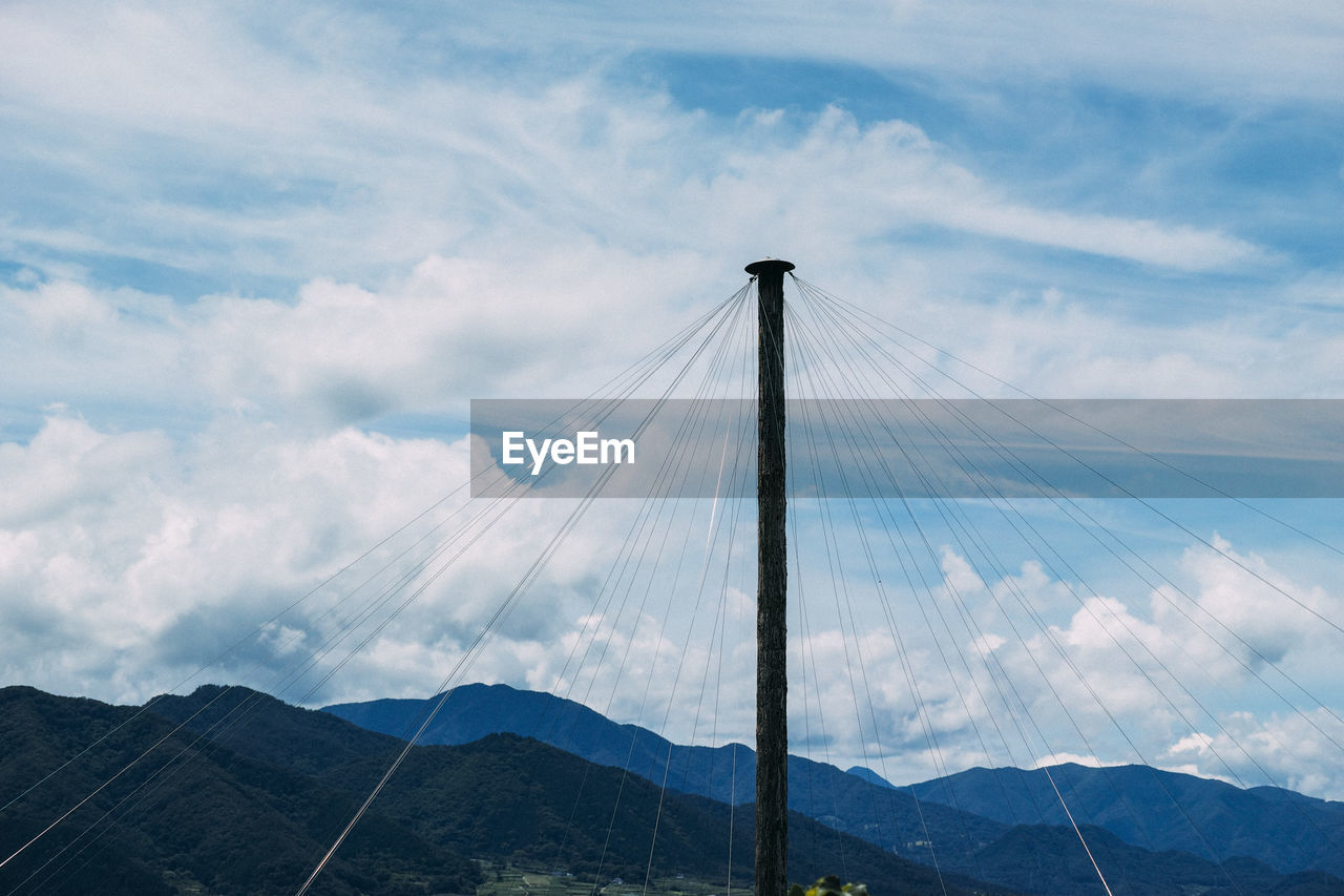 Low angle view of cables attached to pole against cloudy sky