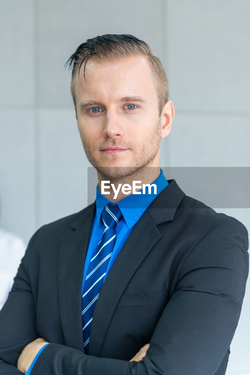 Portrait of businessman with arms crossed standing against wall in office