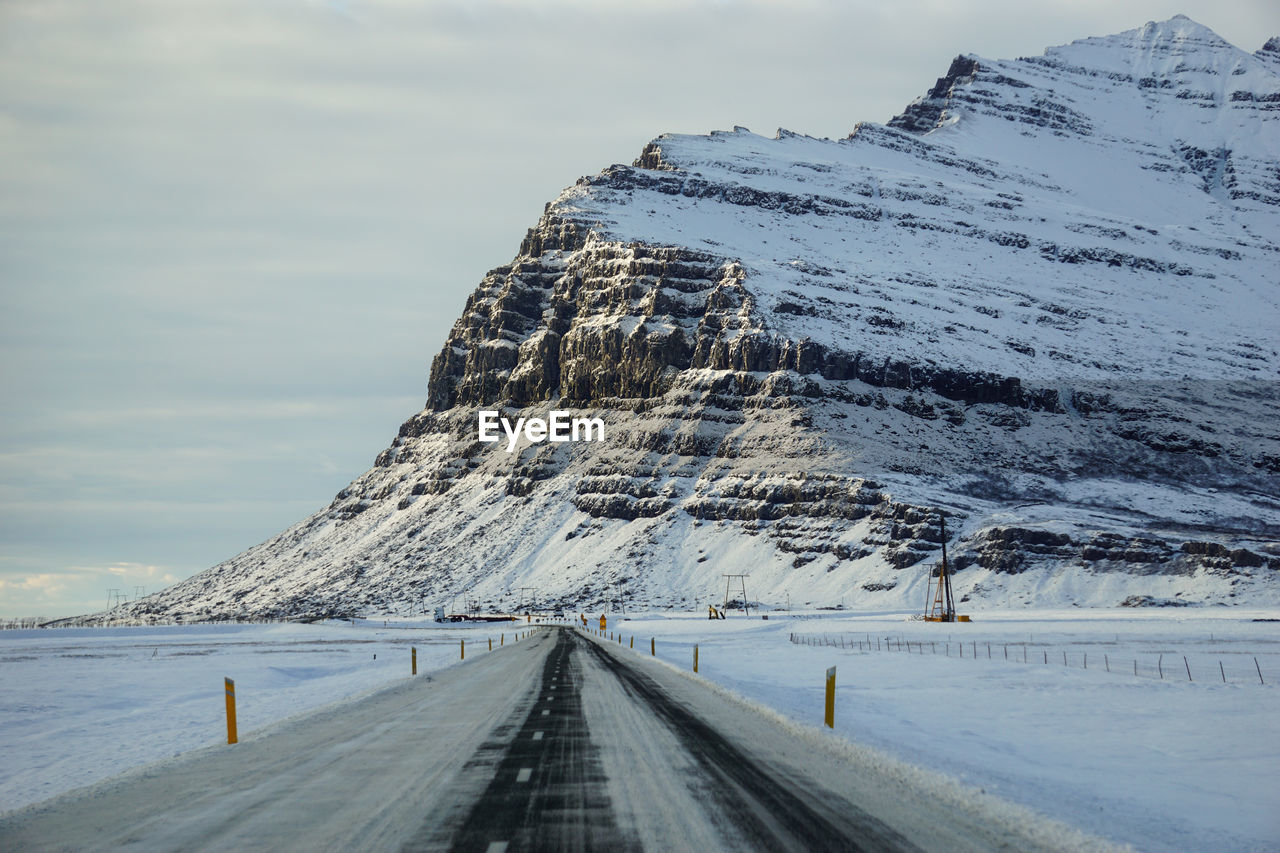 Snow covered road by mountain against sky