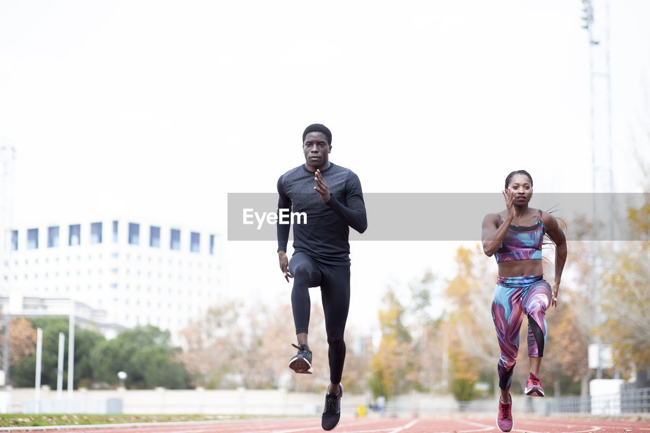 Male and female sportsperson running on track against clear sky