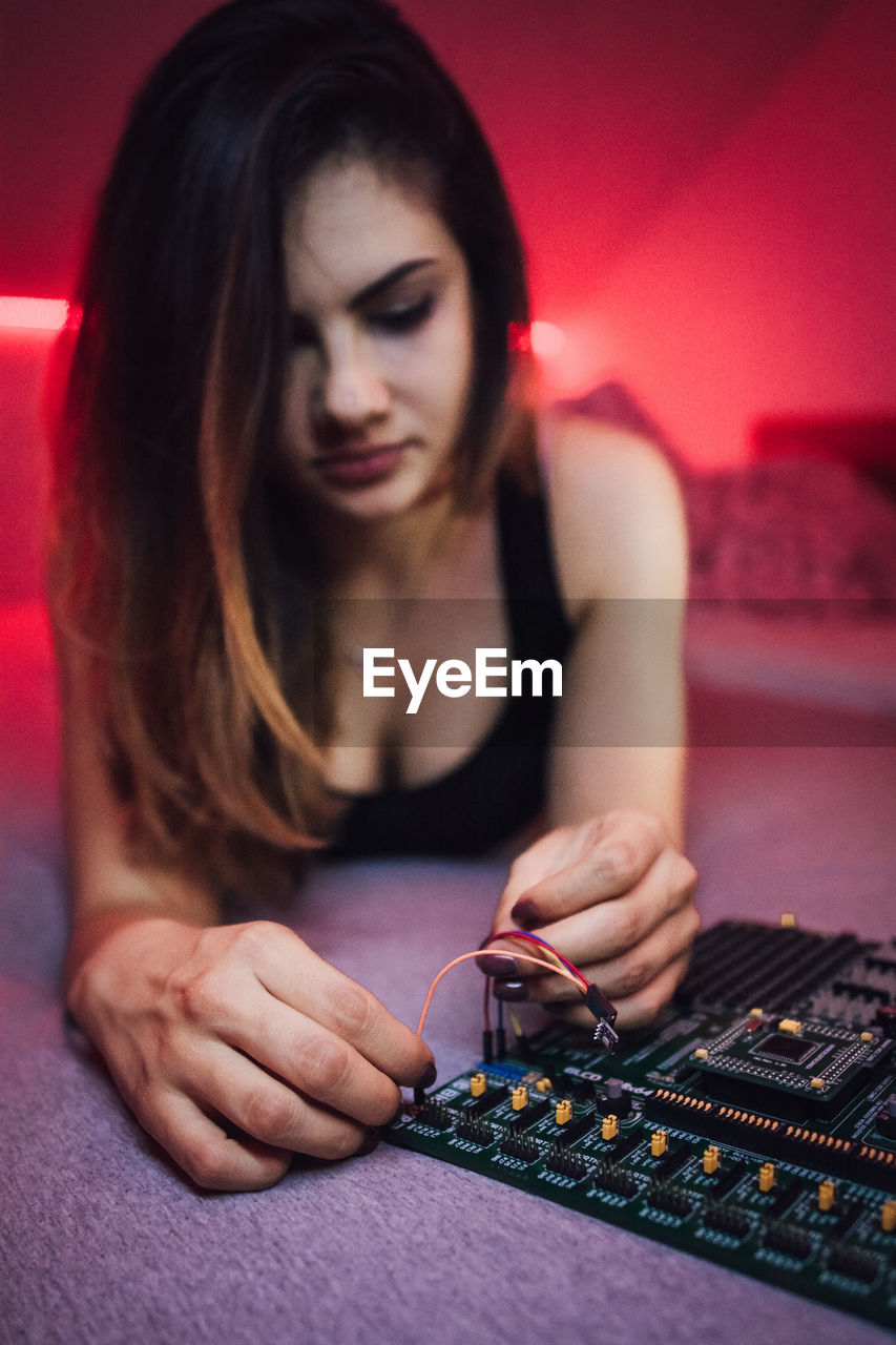 Seductive woman repairing circuit board while lying on bed at home