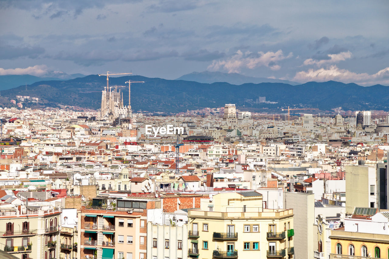 High angle view of townscape and silhouette of sagrada familia against sky, barcelona 