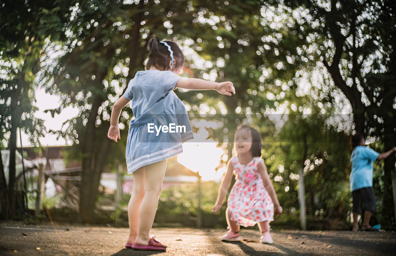 Siblings playing on road by trees