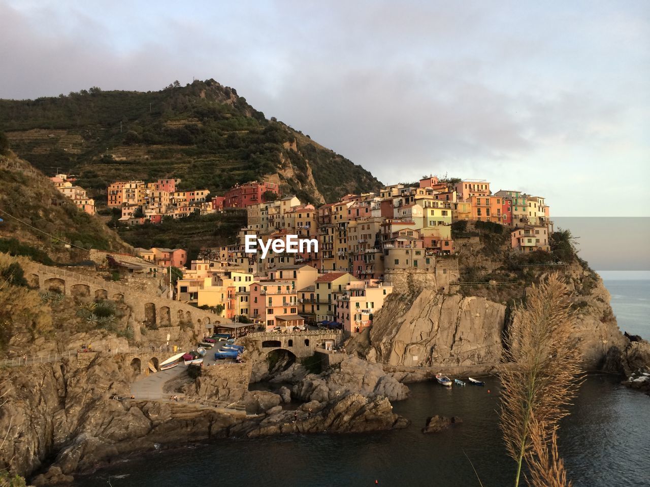 Manarola on mountain at sea shore against sky during sunset