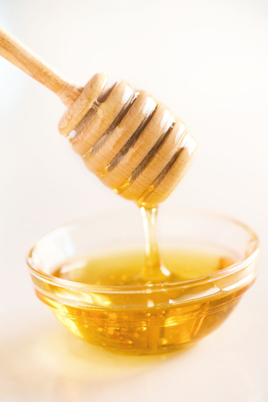 Close-up of honey falling in bowl from dipper against white background