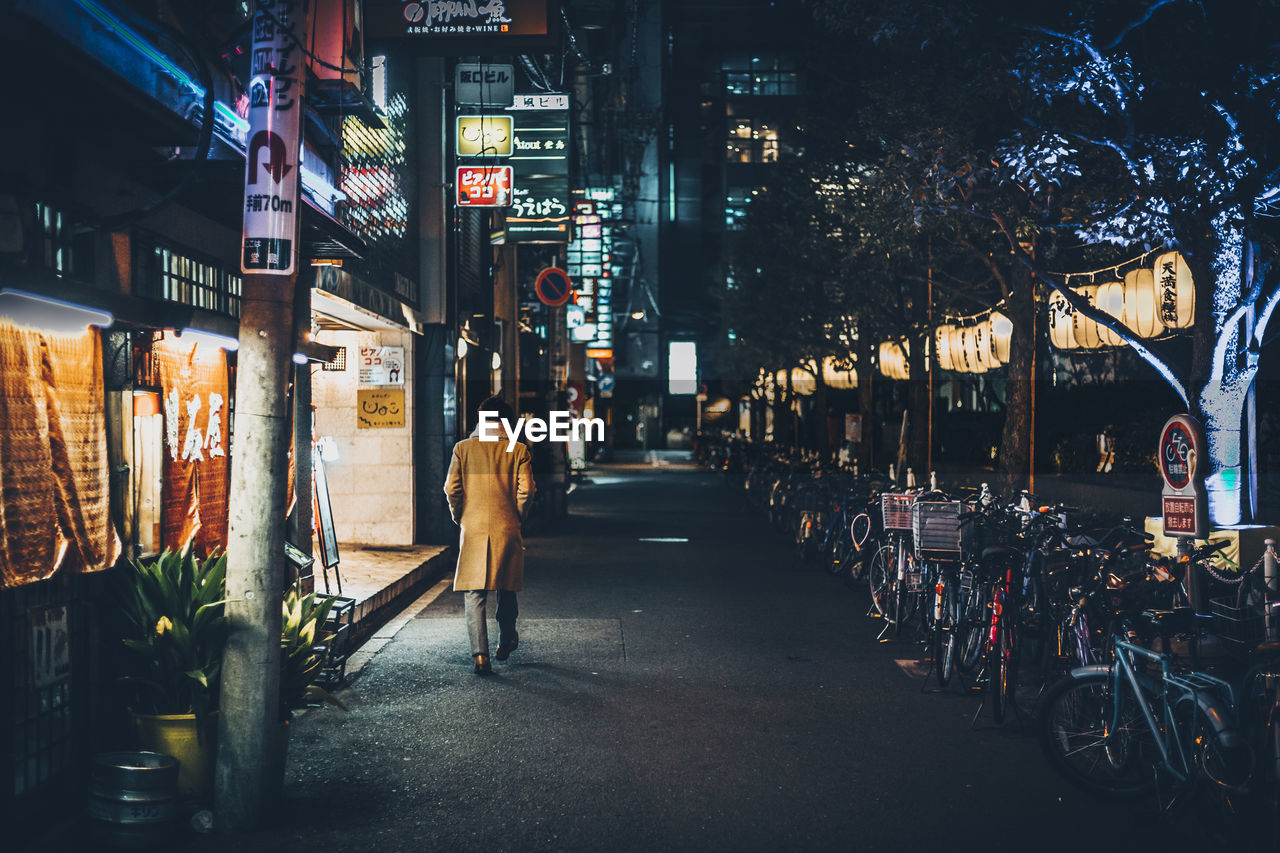 Rear view of man walking on city street at night