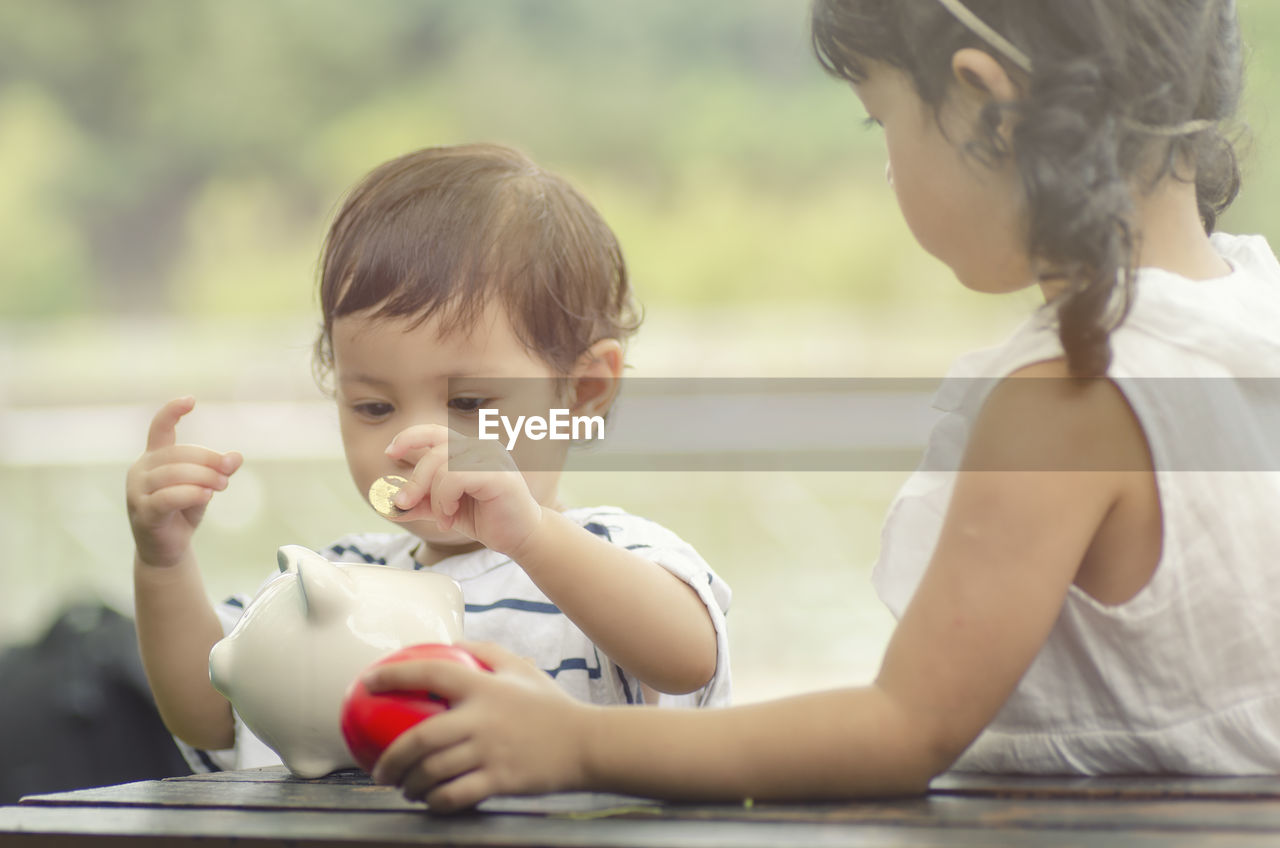 Baby boy with sister inserting coin in piggy bank